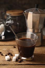 Photo of Brewed coffee in glass, moka pot, beans and sugar cubes on wooden table