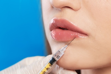 Photo of Young woman getting lips injection on color background, space for text. Cosmetic surgery