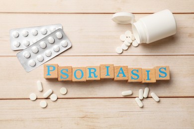 Photo of Word Psoriasis made of cubes with letters and pills on wooden table, flat lay