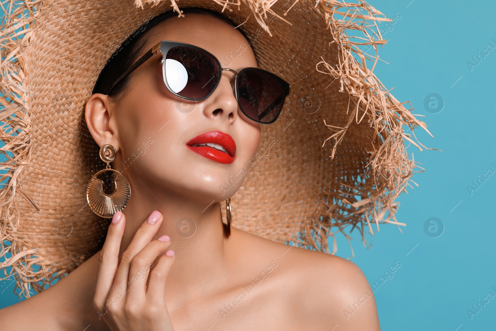 Attractive woman in fashionable sunglasses and wicker hat against light blue background Photo of Attractive woman in fashionable sunglasses and wicker hat against light blue background