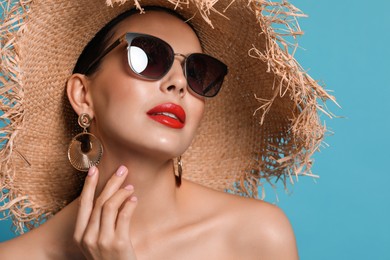 Photo of Attractive woman in fashionable sunglasses and wicker hat against light blue background