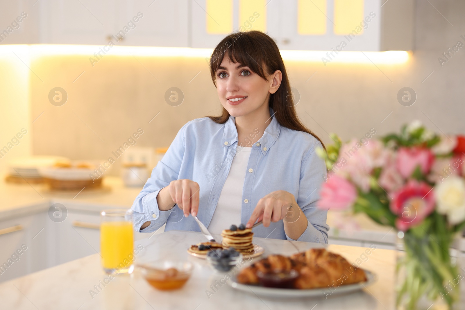 Photo of Smiling woman eating tasty pancakes at breakfast indoors