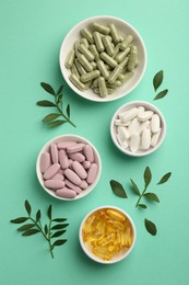 Photo of Different vitamin capsules in bowls and leaves on turquoise background, flat lay