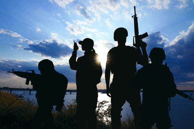 Image of Silhouettes of soldiers with assault rifles and portable radio transmitter patrolling outdoors. Military service