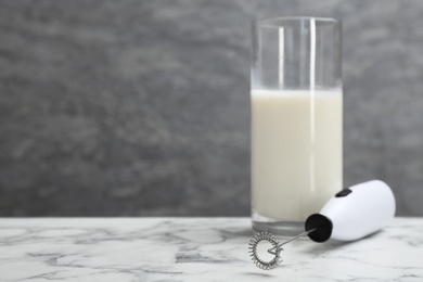 Photo of Milk frother device and glass on table against grey wall. Space for text