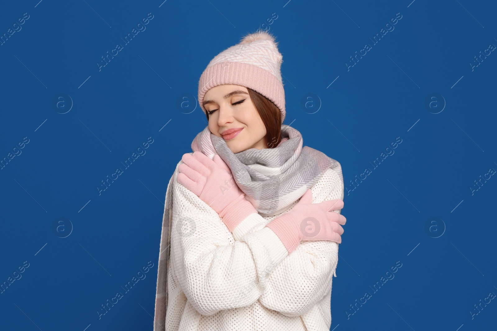 Photo of Young woman wearing warm sweater, gloves, scarf and hat on blue background. Winter season