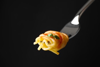 Photo of Fork with tasty pasta on black background, closeup