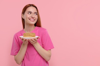 Photo of Young woman with piece of tasty cake on pink background, space for text