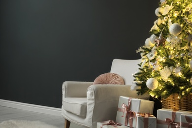 Photo of Beautifully decorated Christmas tree, gift boxes and armchair near black wall indoors, space for text