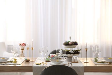 Photo of Beautiful Easter table setting with burning candles and floral decor indoors