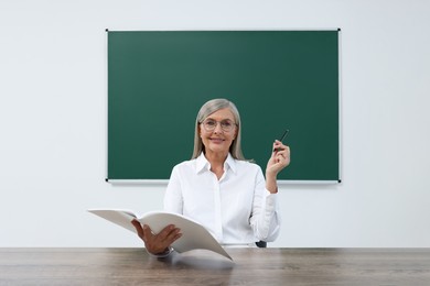 Photo of Professor with notebook and pen sitting at desk in classroom