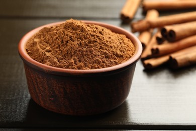 Photo of Bowl of cinnamon powder and sticks on wooden table, closeup
