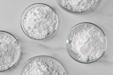 Photo of Many petri dishes with calcium carbonate powder on white marble table, flat lay