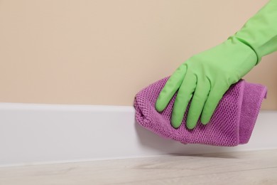 Photo of Woman in protective glove cleaning plinth with washcloth indoors, closeup. Space for text