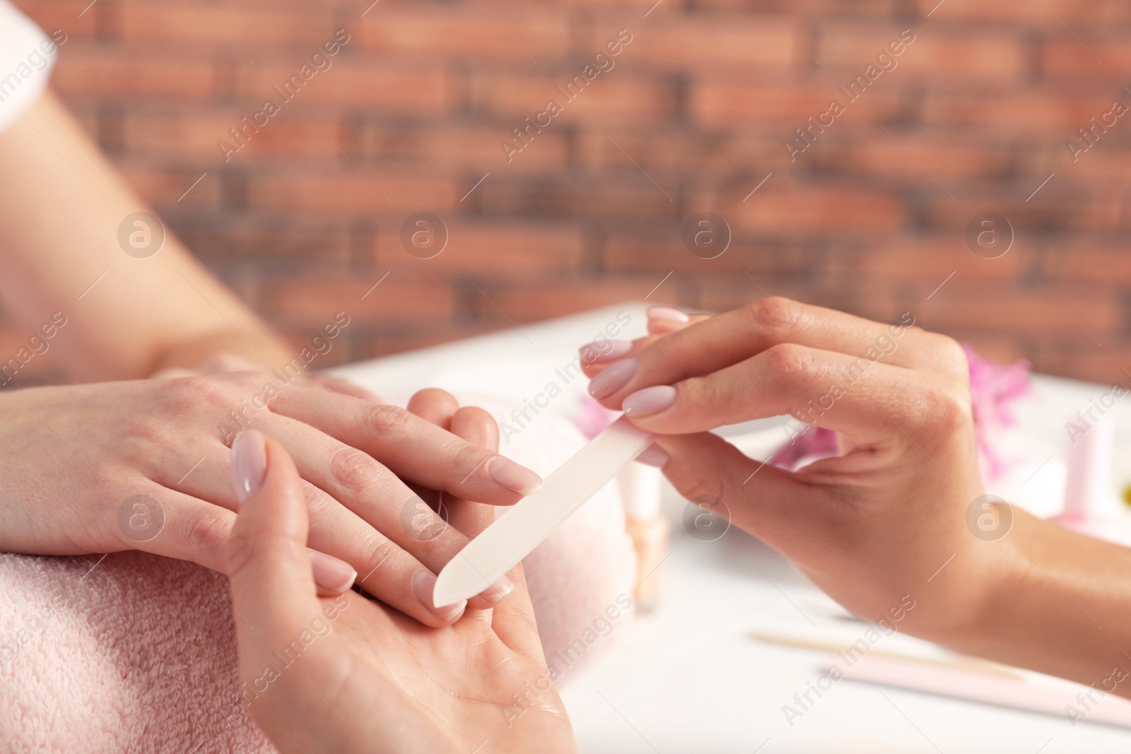 Photo of Manicurist filing client's nails at table, closeup with space for text. Spa treatment