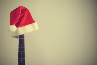 Photo of Guitar with Santa hat on light background, space for text. Christmas music