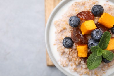 Photo of Tasty wheat porridge with pumpkin, dates and blueberries in bowl on light gray table, top view. Space for text