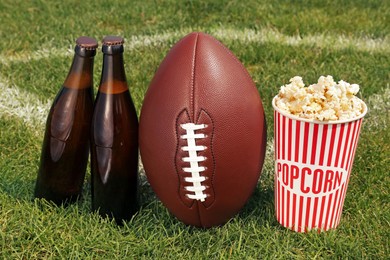 Photo of American football ball with beer and popcorn on green field grass