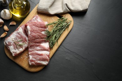 Photo of Raw ribs with rosemary and salt on black table, flat lay. Space for text