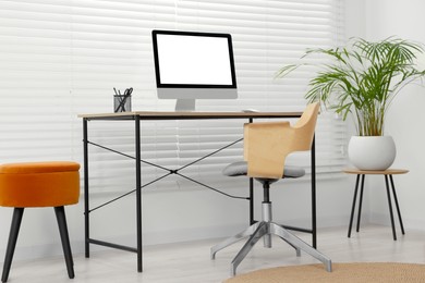 Photo of Stylish office interior with comfortable chair, desk, computer and houseplant