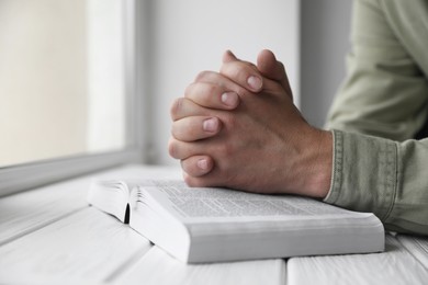 Photo of Religion. Christian man praying over Bible at white wooden the table, closeup