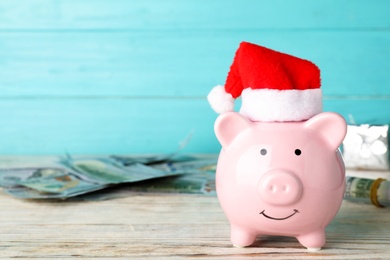 Photo of Piggy bank with Santa hat and dollar banknotes on table. Space for text