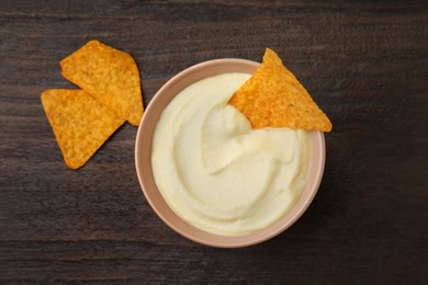 Photo of Delicious tofu sauce served with nachos chips in bowl on wooden table, top view