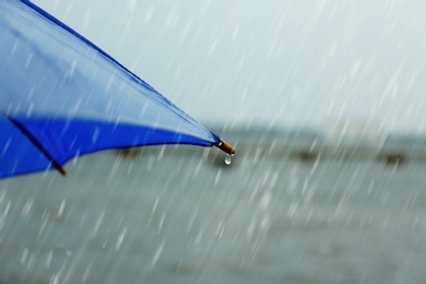 Photo of Blue umbrella under rain near river, closeup view