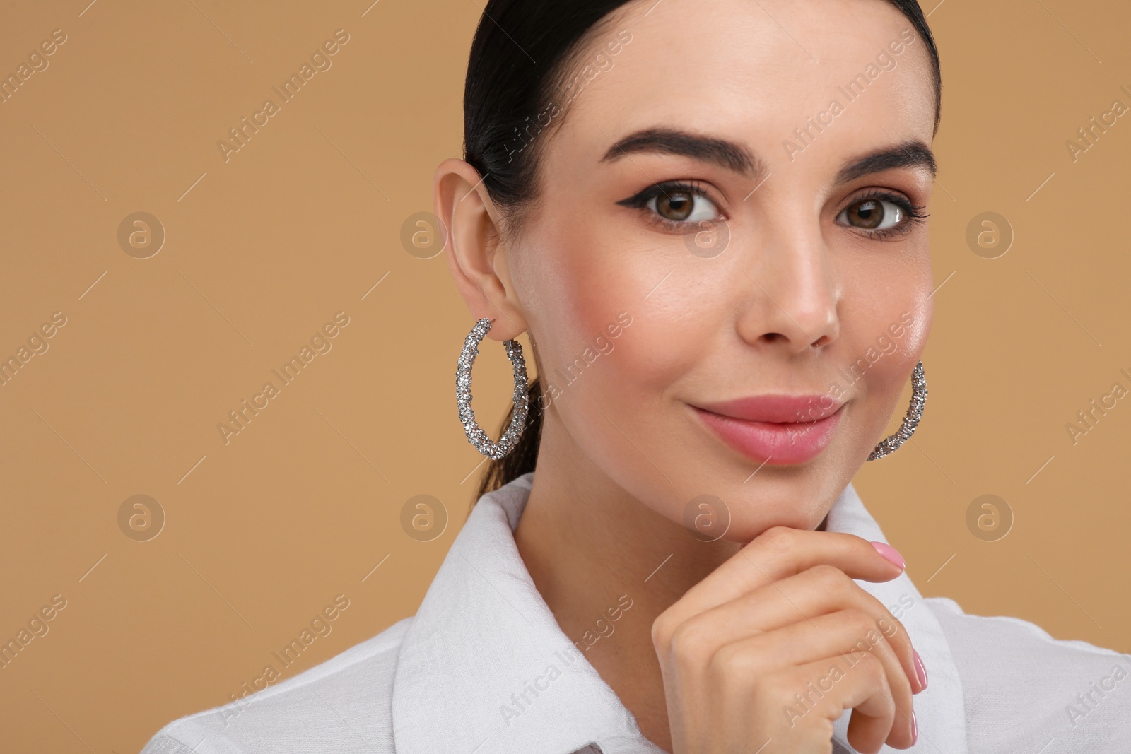 Photo of Beautiful young woman with elegant earrings on beige background, closeup