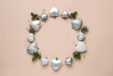 Photo of Beautiful festive wreath made of heart shaped Christmas balls and fir tree branches on beige background, top view