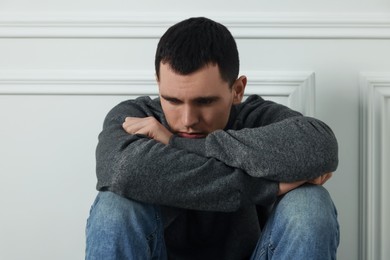 Photo of Sad man sitting near white wall indoors