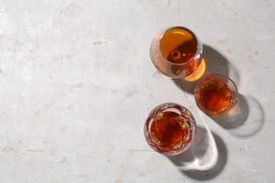 Photo of Different delicious liqueurs in glasses on light grey table, flat lay. Space for text