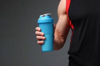 Photo of Young man with muscular body holding shaker of protein on grey background, closeup. Space for text