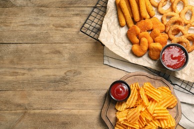 Photo of Tasty ketchup and different snacks on wooden table, flat lay. Space for text