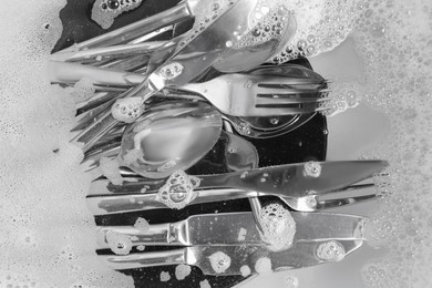 Photo of Washing silver spoons, forks and knives in water with foam, flat lay