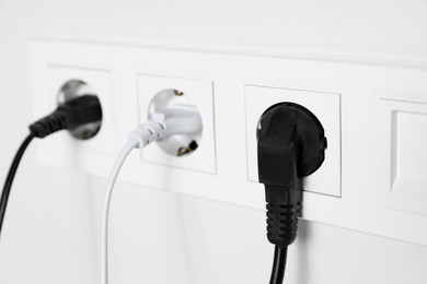 Photo of Power sockets with inserted plugs on white wall, closeup. Electrical supply