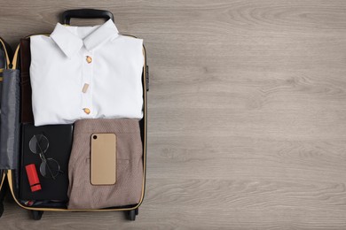 Photo of Folded clothes and accessories in open suitcase on wooden background, top view with space for text. Business trip preparations