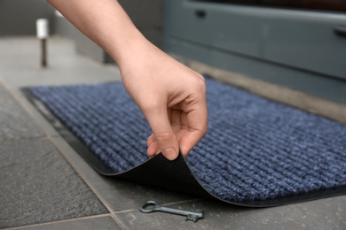 Photo of Woman's hand lifting door mat to reveal key hidden underneath, closeup