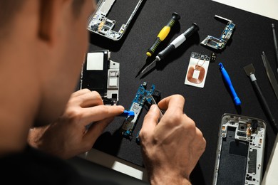 Photo of Technician repairing broken smartphone at table, closeup