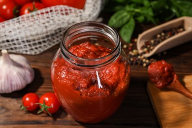 Jar of tasty tomato paste and ingredients on wooden table, closeup