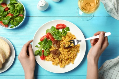 Photo of Woman eating rice pilaf with meat and salad at table, top view