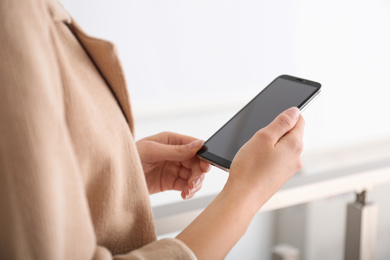 Photo of Young woman using modern smartphone indoors, closeup