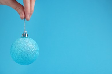 Photo of Woman holding glitter Christmas ball on light blue background, closeup. Space for text