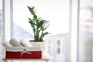 Photo of Basket with towels and houseplant on table near window