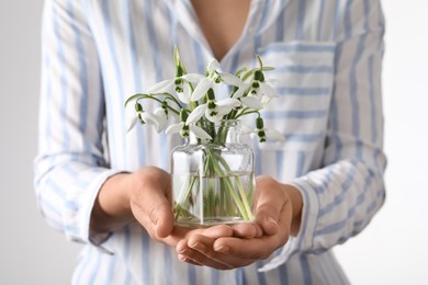 Photo of Woman holding glass jar with snowdrops on light background, closeup