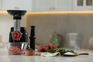 Photo of Electric meat grinder with beef mince, parsley, salt and peppercorns on white table in kitchen