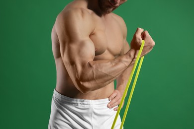 Photo of Muscular man exercising with elastic resistance band on green background, closeup
