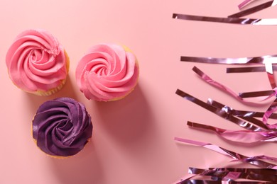 Photo of Delicious cupcakes with bright cream and confetti on pink background, flat lay