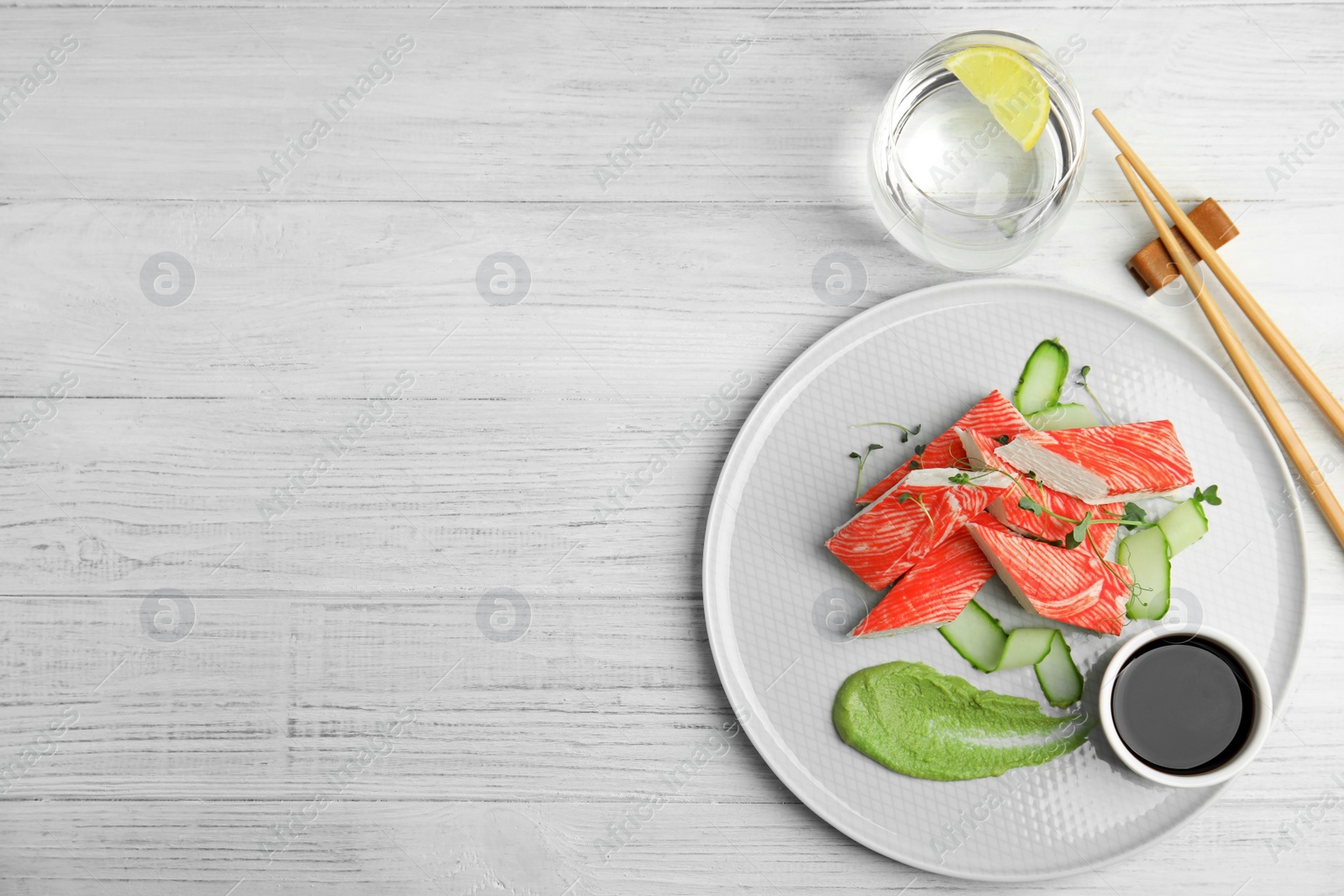 Photo of Fresh crab sticks with cucumber and soy sauce served on white wooden table, flat lay. Space for text