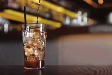 Photo of Pouring cola into glass with ice cubes on table indoors. Space for text